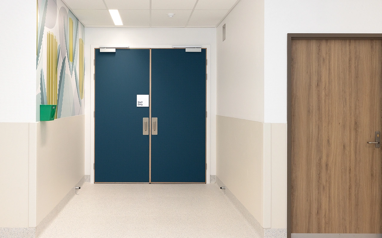 A clean hallway with white walls, a wooden door on the right, and double blue doors marked "Staff Only" at the end. A green box and abstract wall art are visible on the left.
