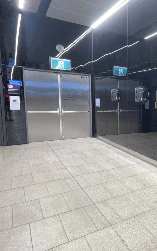 Corridor with stainless steel double doors labeled 'Staff Only', bright exit signs, and a mirrored wall.