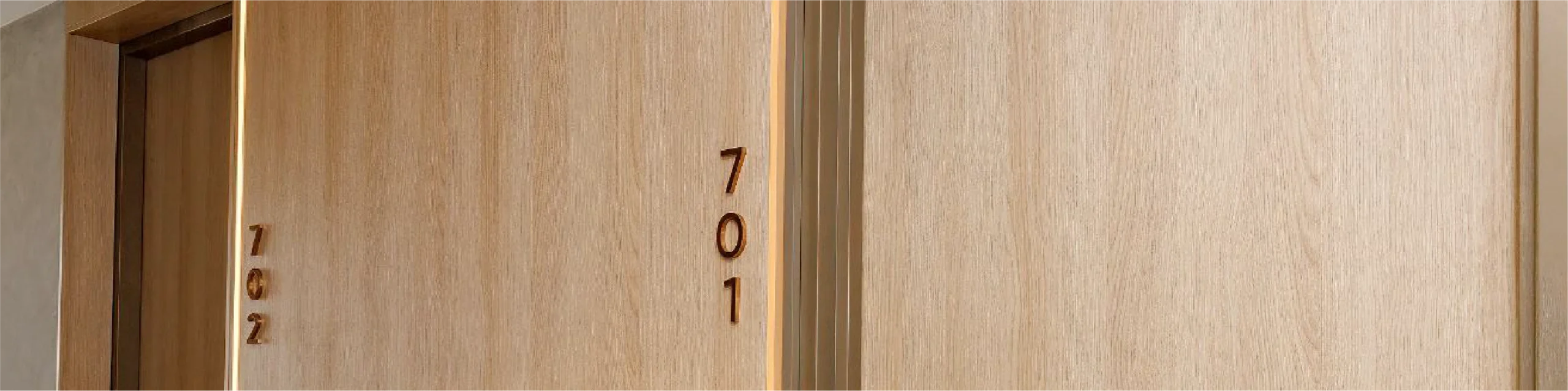 Close-up of two light wood Fire-rated Doors Sydney, vertically aligned with room numbers 701 and 702.