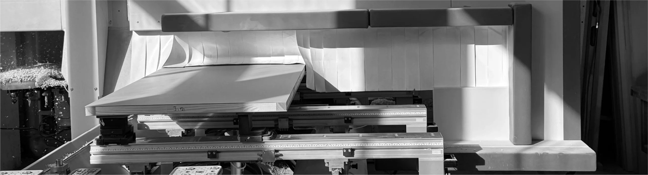 Wooden board on metal automated machine in workshop, natural light, part of Non Rated Doors fabrication process.